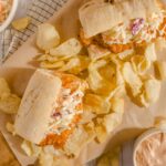 Decadent fried chicken sandwich with coleslaw and potato chips, served with creamy dipping sauce on a rustic wooden board. Perfect comfort food featuring crispy chicken, fresh coleslaw, and crunchy chips.