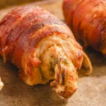Juicy bacon-wrapped stuffed chicken roll loaded with melted cheese on a rustic baking sheet for delicious homemade meal.