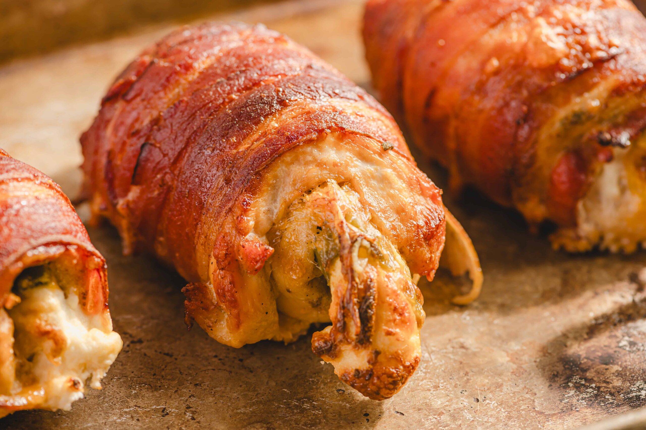 Juicy bacon-wrapped stuffed chicken roll loaded with melted cheese on a rustic baking sheet for delicious homemade meal.