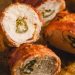 Juicy chicken breast roulades stuffed with cheese and jalapeno peppers, wrapped in crispy bacon, cooked to perfection, and sliced to reveal flavorful filling, served on a rustic baking sheet.