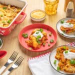 Crispy baked chicken enchiladas with melted cheese and fresh green onions on a white plate, served with sour cream and side dishes, on a wooden table with cutlery and condiments, delicious and cheesy Tex-Mex comfort food.