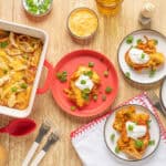 Crispy baked chicken casserole with melted cheese and scallions, served with sour cream and green onions on a wooden table for a comforting home-cooked meal.