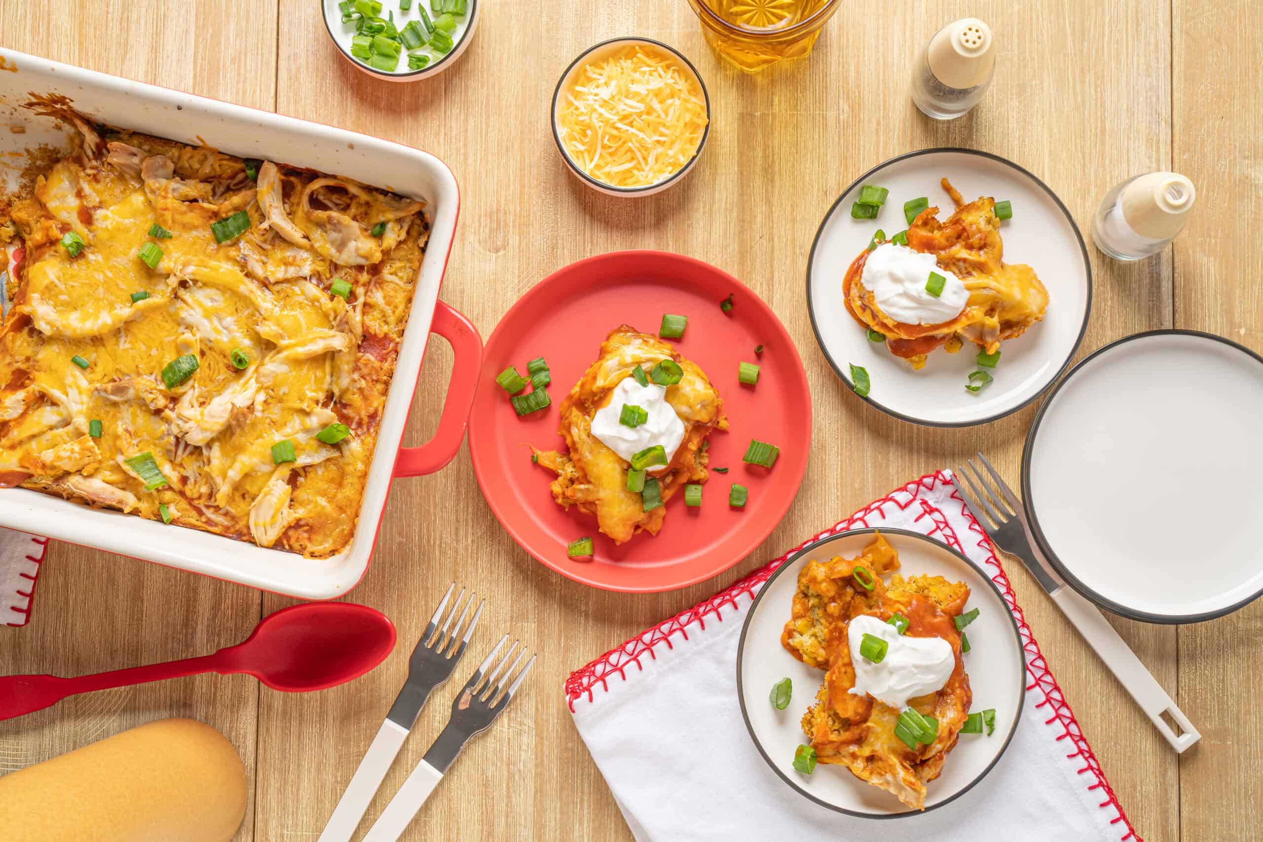 Crispy baked chicken casserole with melted cheese and scallions, served with sour cream and green onions on a wooden table for a comforting home-cooked meal.