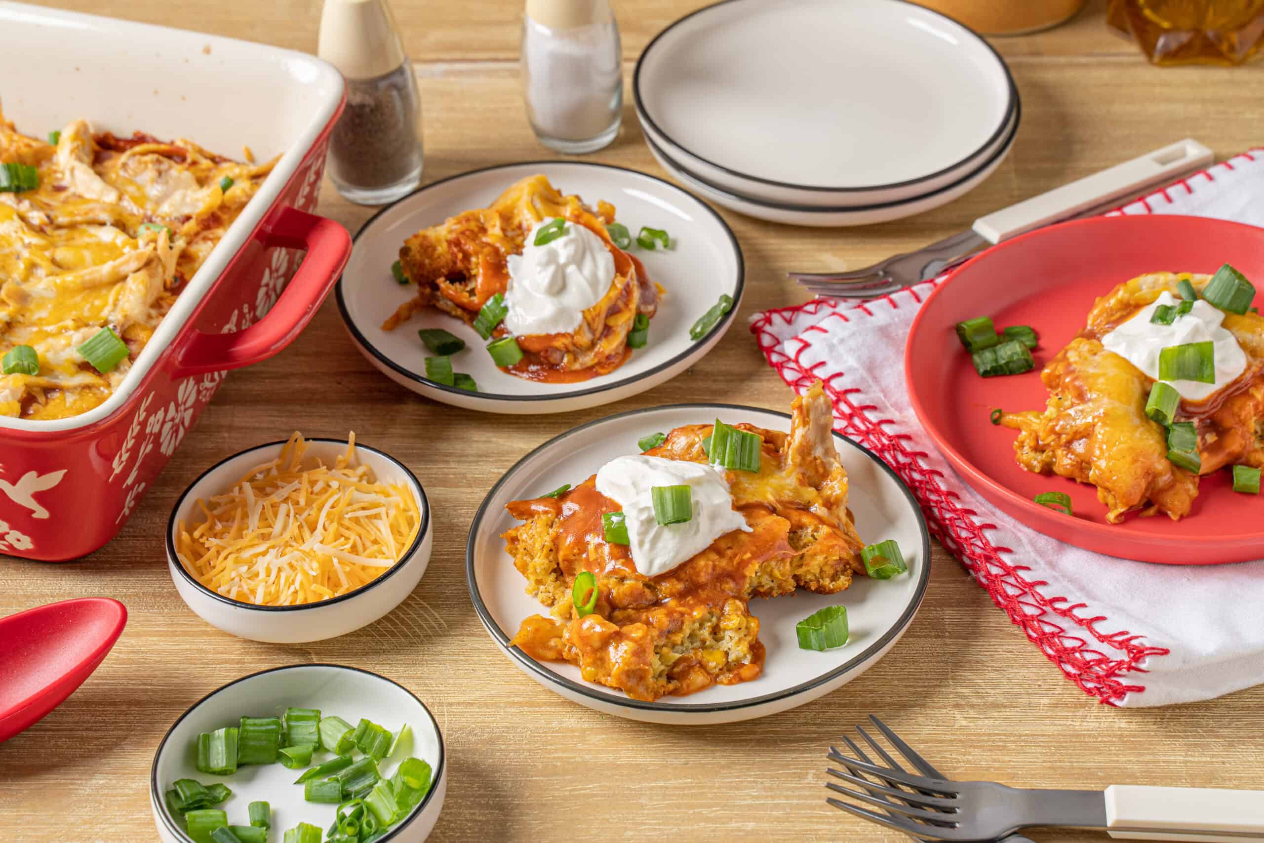 Creamy chicken and cheese casserole with sour cream and green onions, served with shredded cheese and fresh chopped scallions on a wooden table.