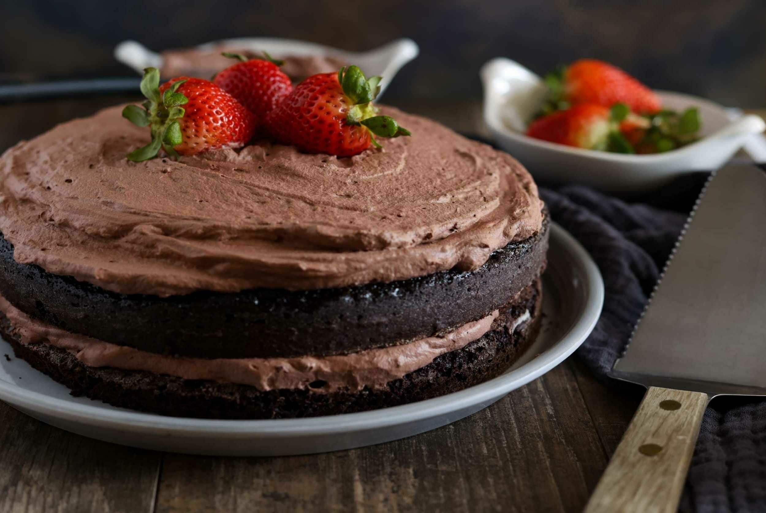 Chocolate cake with strawberry topping on a white plate, served with fresh strawberries in a small bowl, perfect for dessert or special occasions.