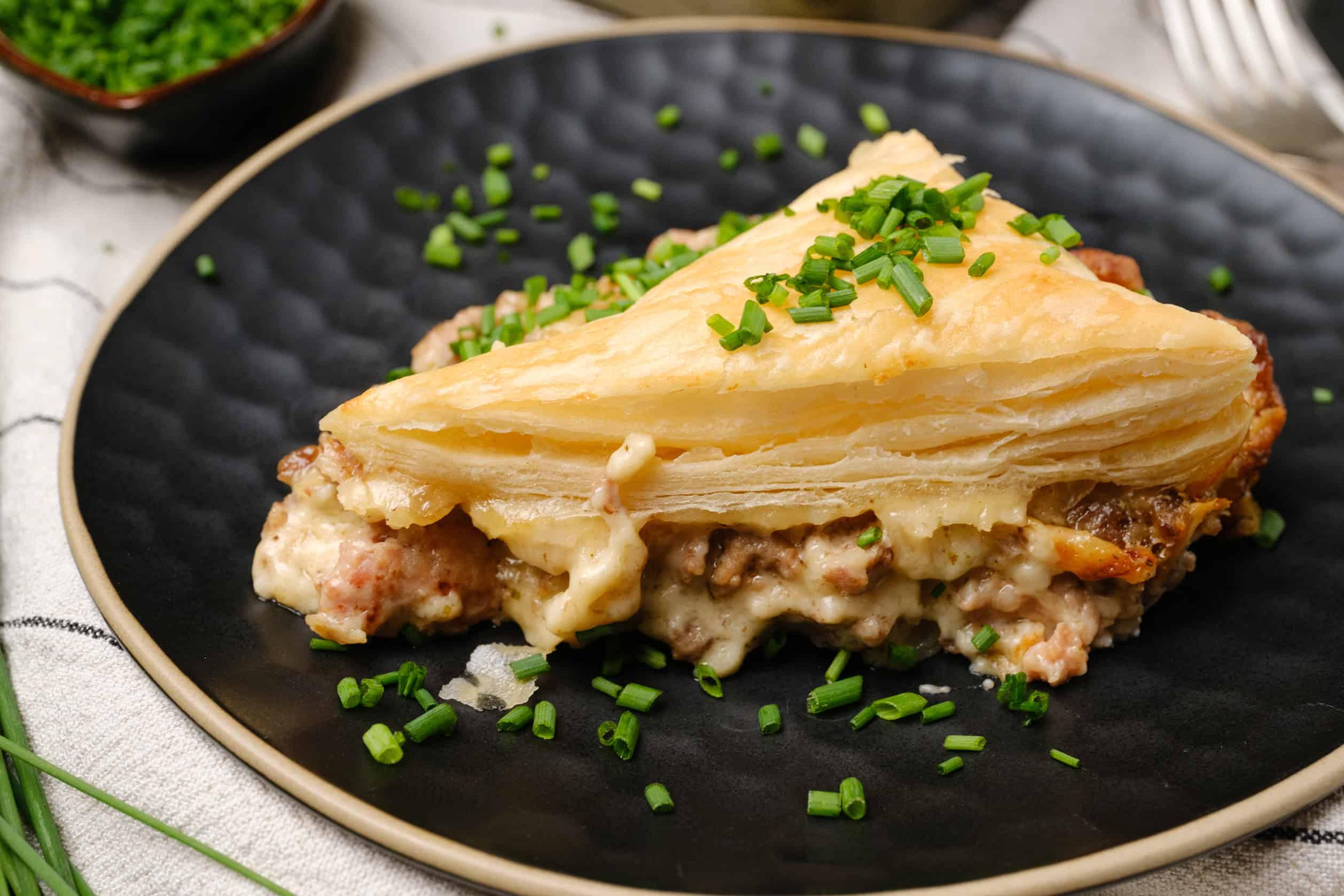 Creamy chicken pot pie with flaky pastry crust on black ceramic plate, garnished with chopped green onions, served with fresh herbs on side, comfort food idea.