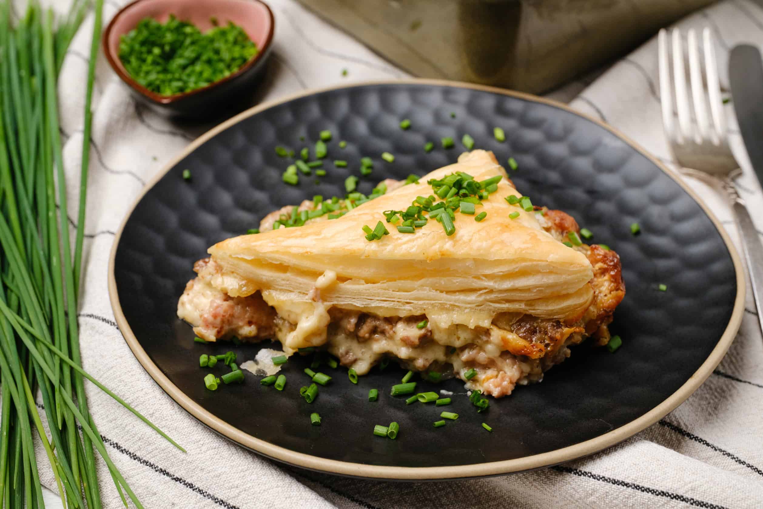 Creamy chicken and mushroom pot pie with a flaky puff pastry crust garnished with chopped chives, served on a stylish black plate. Perfect comfort food with savory filling and golden crust.