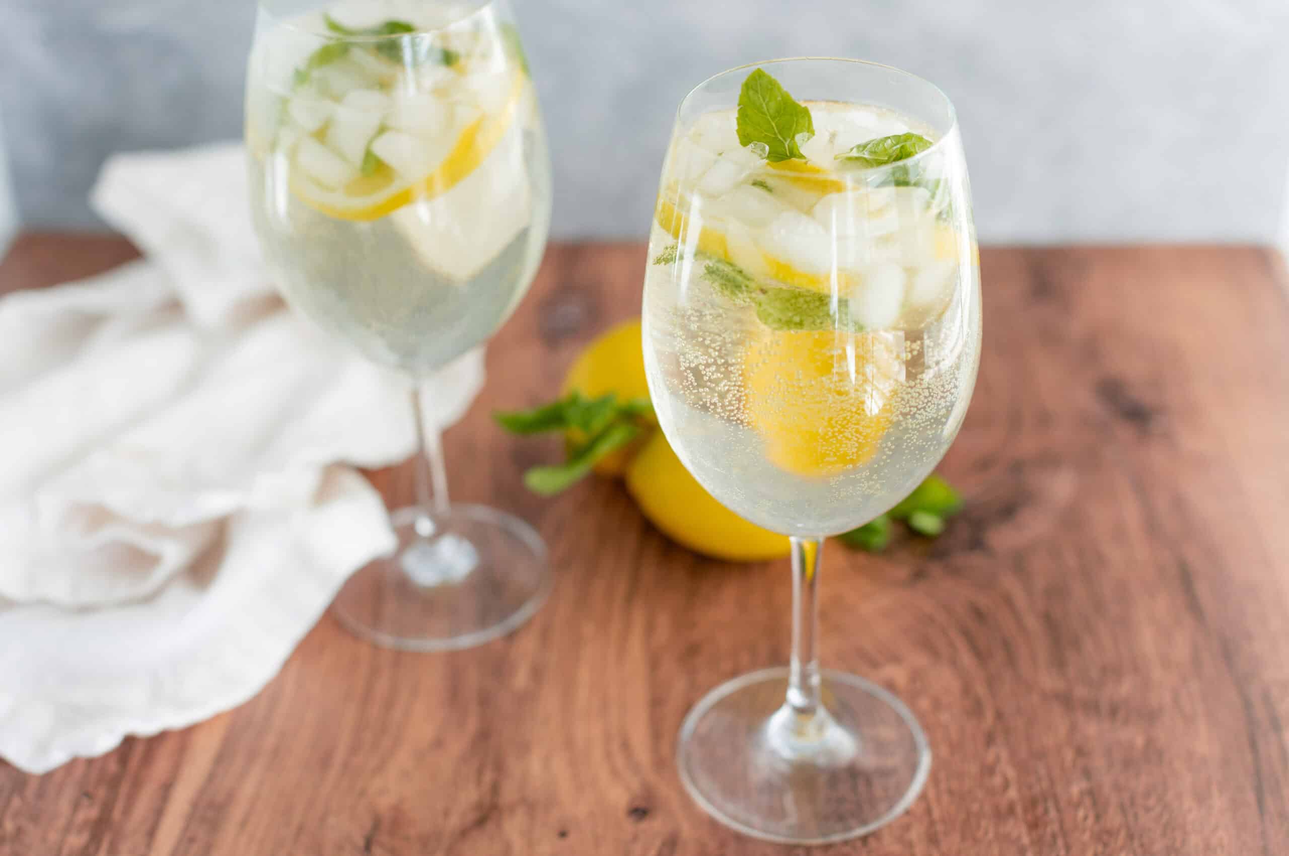 Refreshing lemon mint sparkling water with ice, lemon slices, and fresh mint leaves garnishing chilled glasses on wooden table for a summer drink.