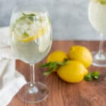 Refreshing lemon and cucumber sparkling water in elegant wine glasses, garnished with fresh lemon slices and mint leaves, served on a rustic wooden table with whole lemons nearby.