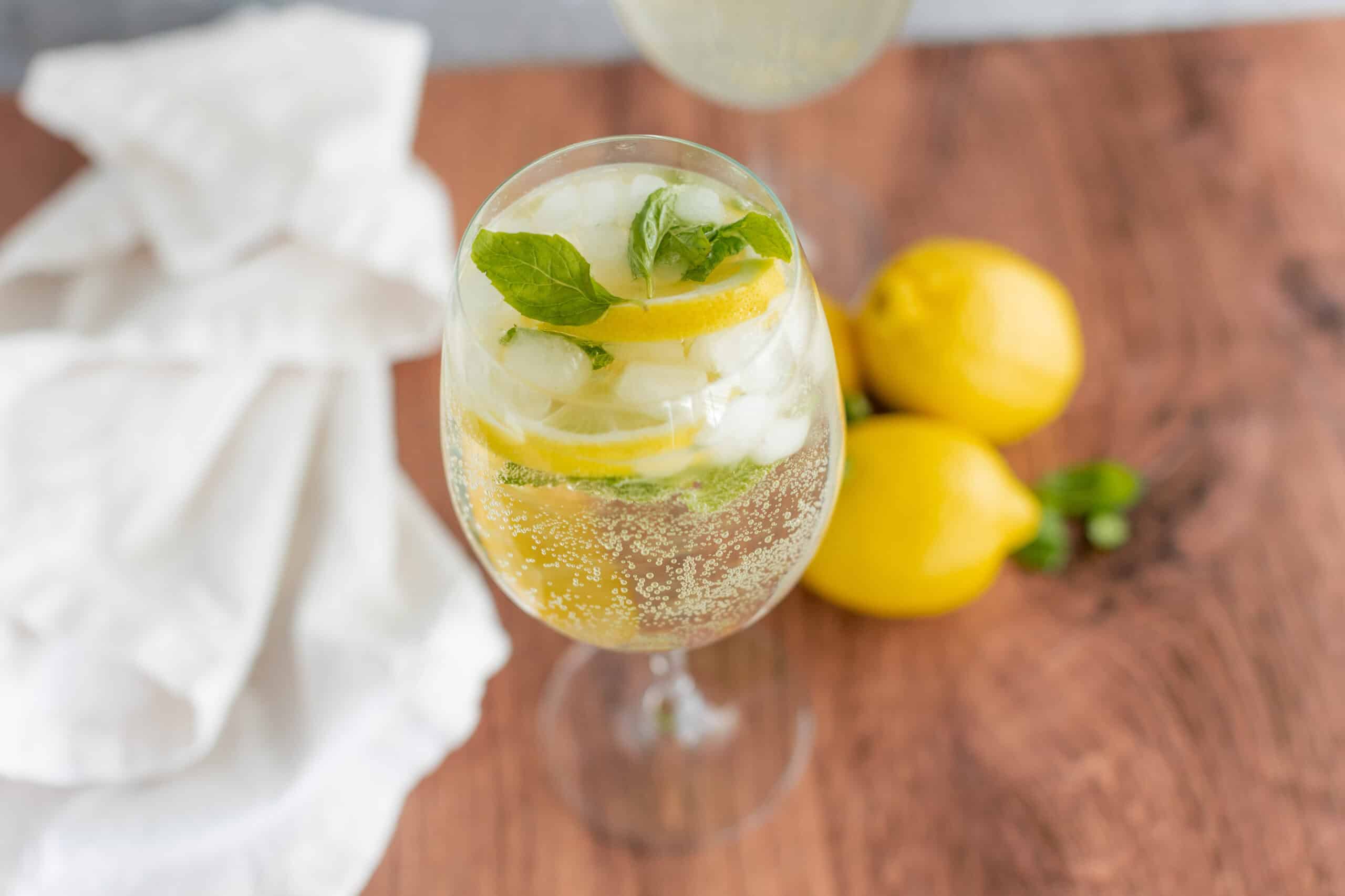 Fresh lemon and mint infused sparkling water with ice in a tall glass, refreshing summer beverage.