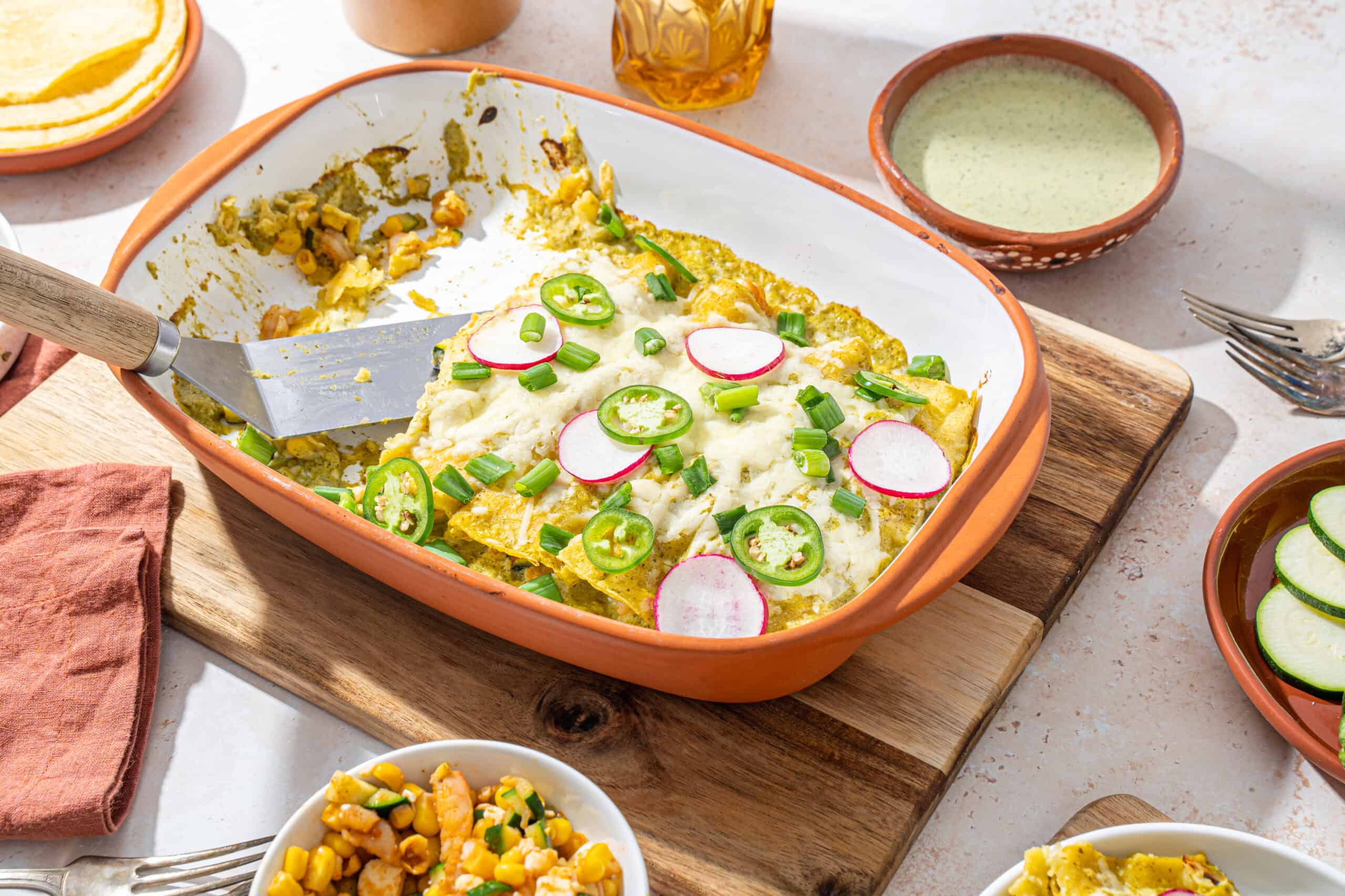Colorful baked casserole with eggs, radishes, and green onions topped with melted cheese in a rustic orange baking dish on a wooden cutting board.