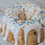Rich vanilla cake with colorful sprinkles and white icing glaze, perfect for birthday celebrations and festive occasions.