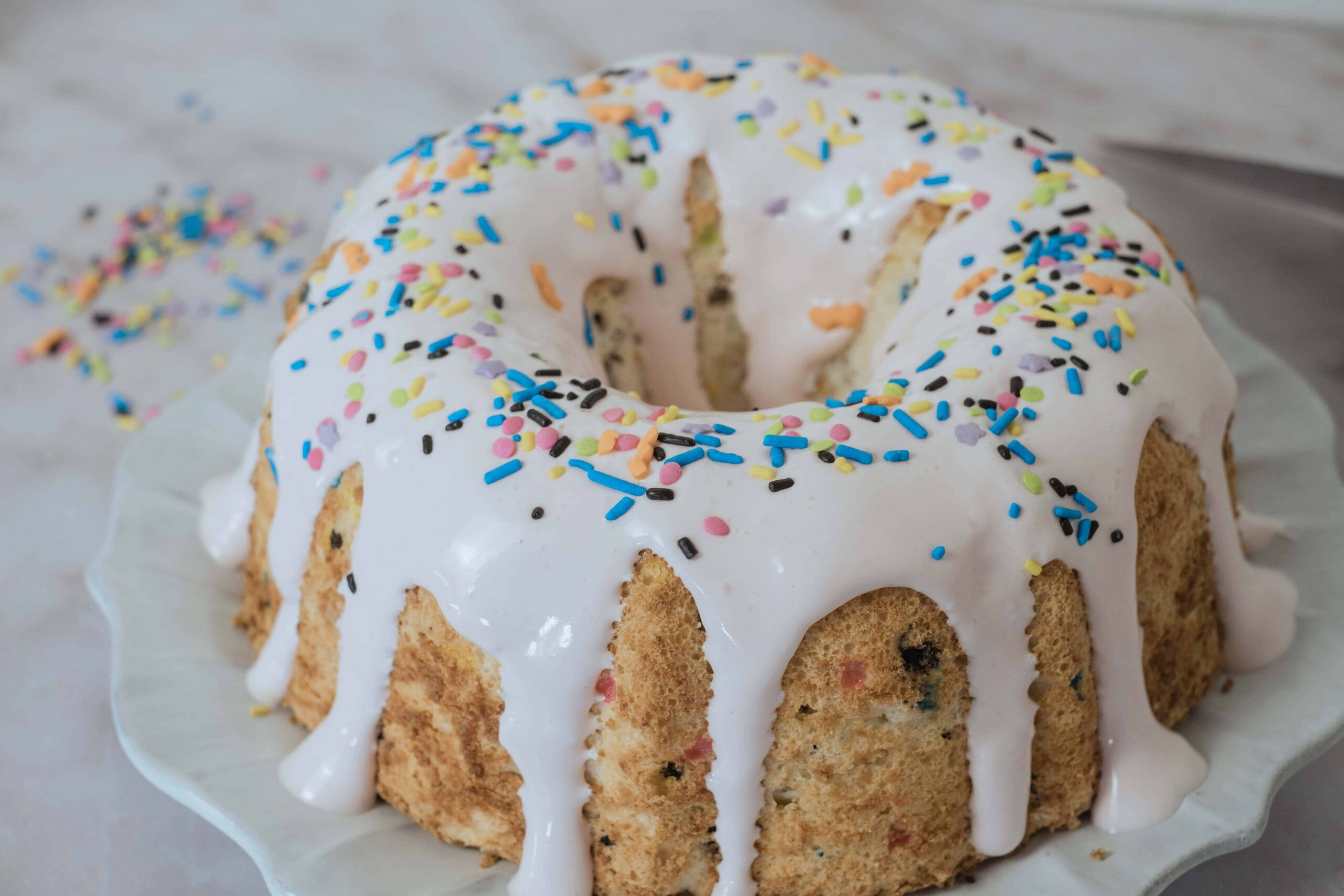 Rich vanilla cake with colorful sprinkles and white icing glaze, perfect for birthday celebrations and festive occasions.