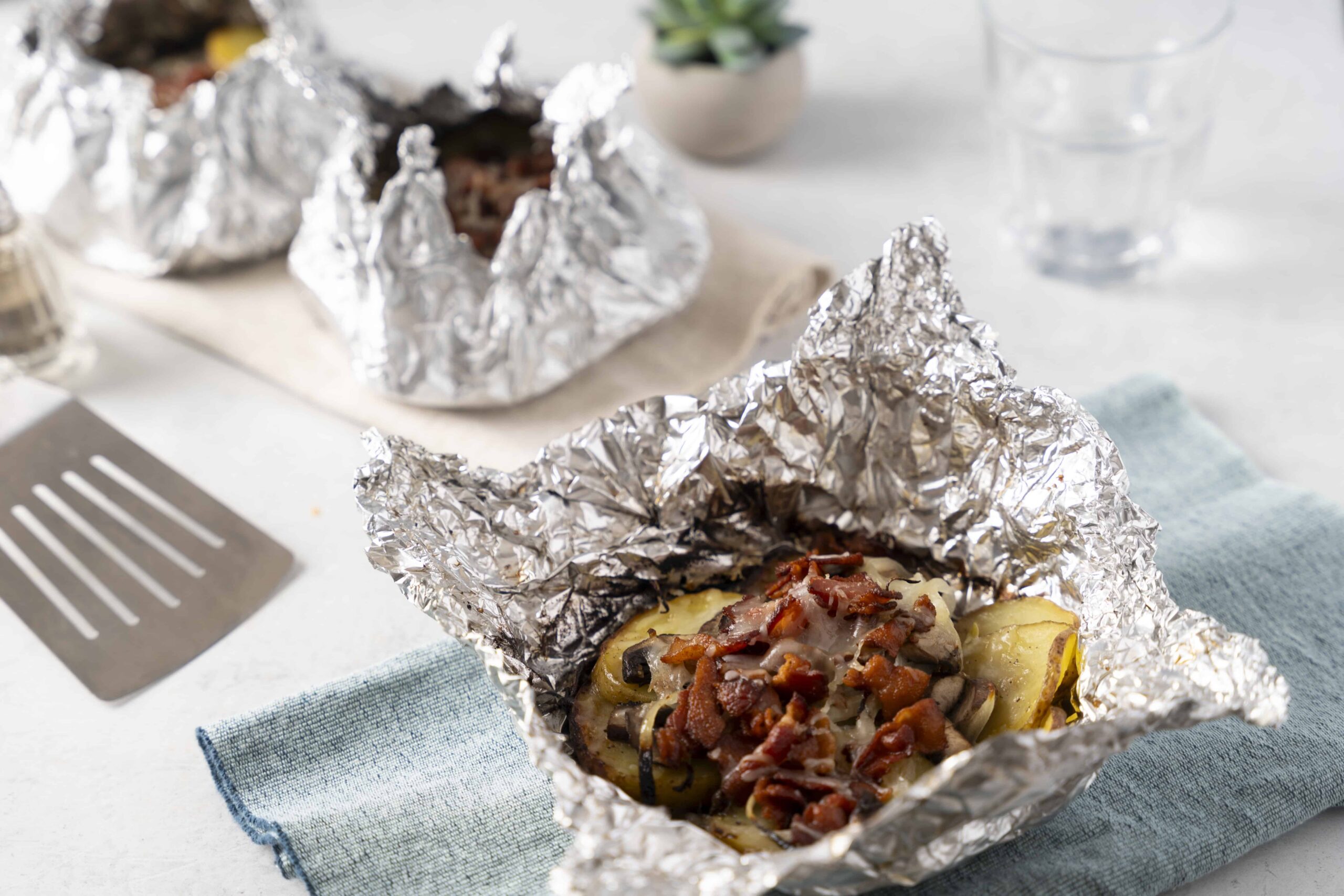 Aluminum foil-wrapped baked potato topped with crispy bacon, onions, and cheese, ready to serve; perfect for a hearty comfort food meal.