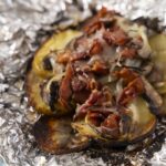 Grilled eggplant topped with crispy bacon, mushrooms, and melted cheese on foil. Healthy and delicious vegetarian steak alternative with savory toppings.