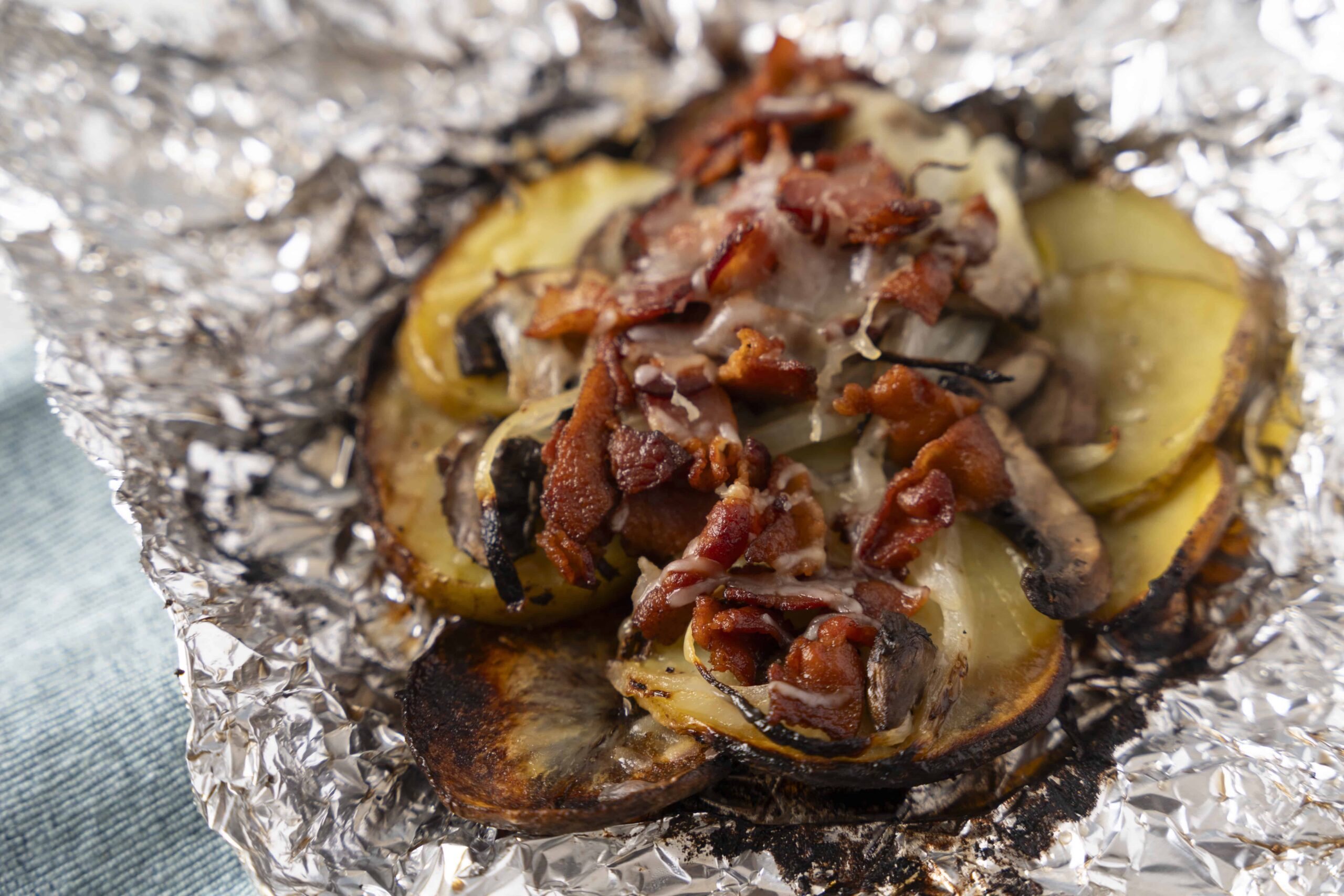 Grilled eggplant topped with crispy bacon, mushrooms, and melted cheese on foil. Healthy and delicious vegetarian steak alternative with savory toppings.