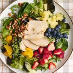 Fresh chicken salad with mixed greens, strawberries, blueberries, pineapple, walnuts, and honey mustard dressing on a white plate.