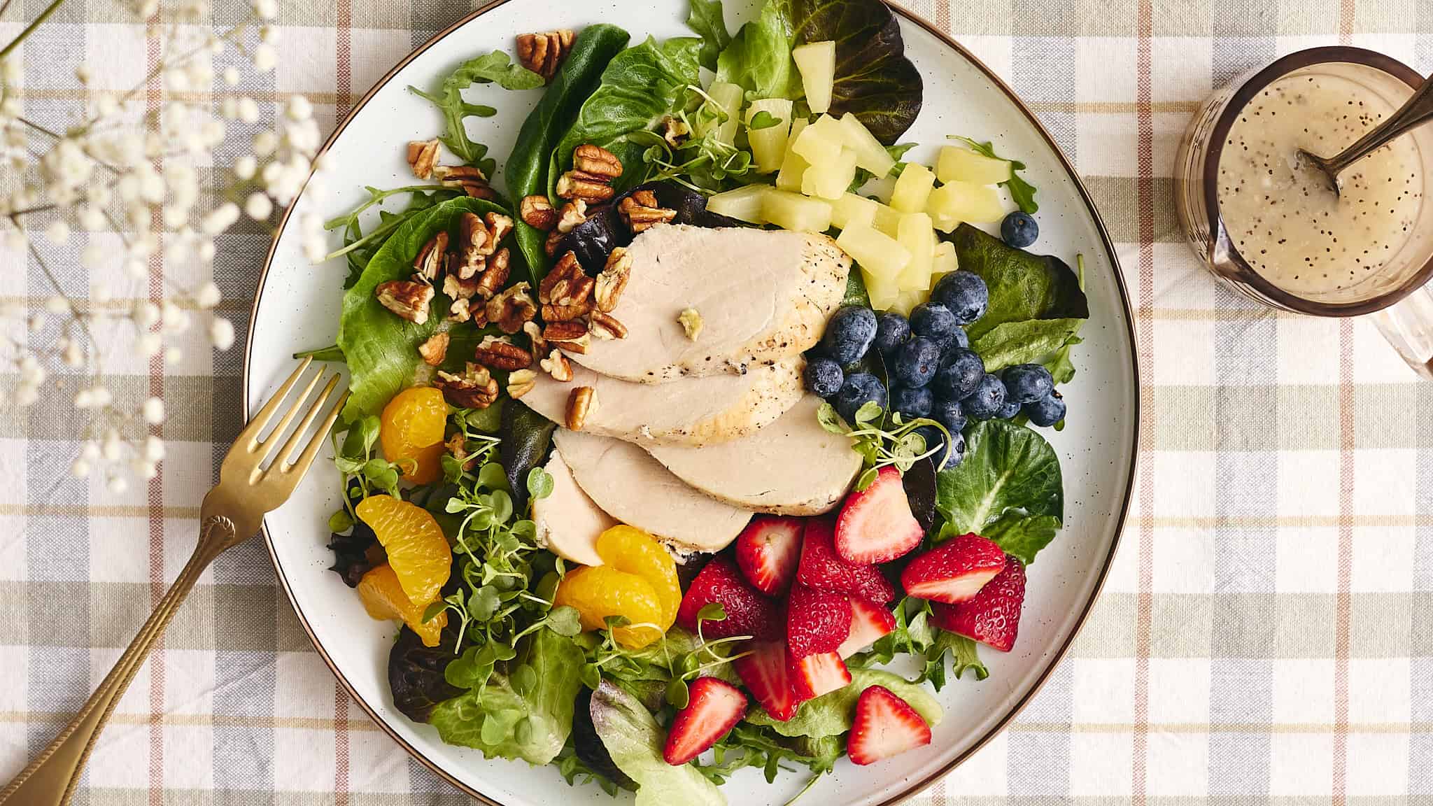 Fresh chicken salad with mixed greens, strawberries, blueberries, pineapple, walnuts, and honey mustard dressing on a white plate.