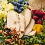 Fresh grilled chicken salad with mixed greens, strawberries, blueberries, pineapple, mandarin oranges, walnuts, and creamy dressing drizzle. Perfect healthy meal for lunch or dinner.