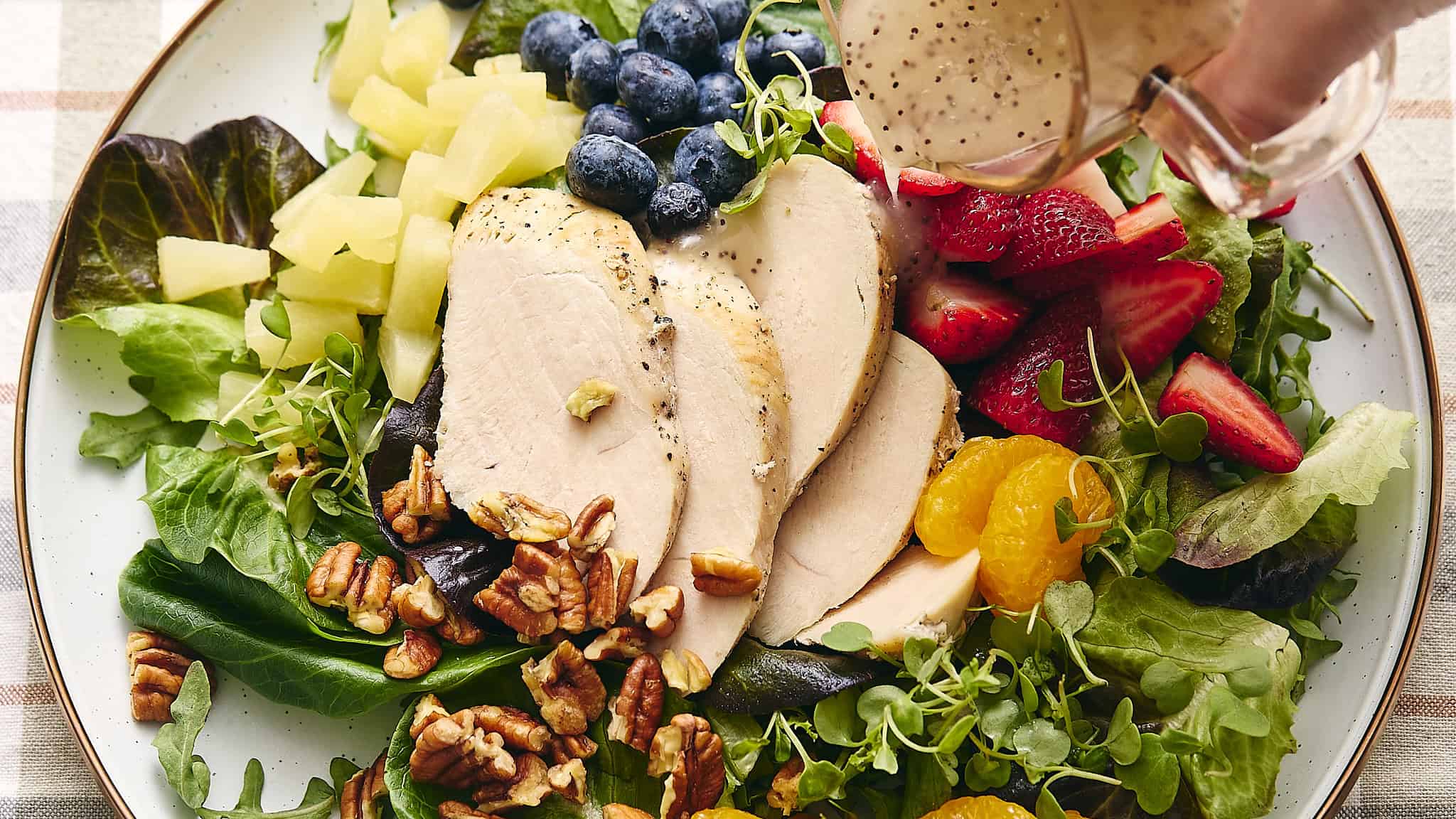 Fresh grilled chicken salad with mixed greens, strawberries, blueberries, pineapple, mandarin oranges, walnuts, and creamy dressing drizzle. Perfect healthy meal for lunch or dinner.