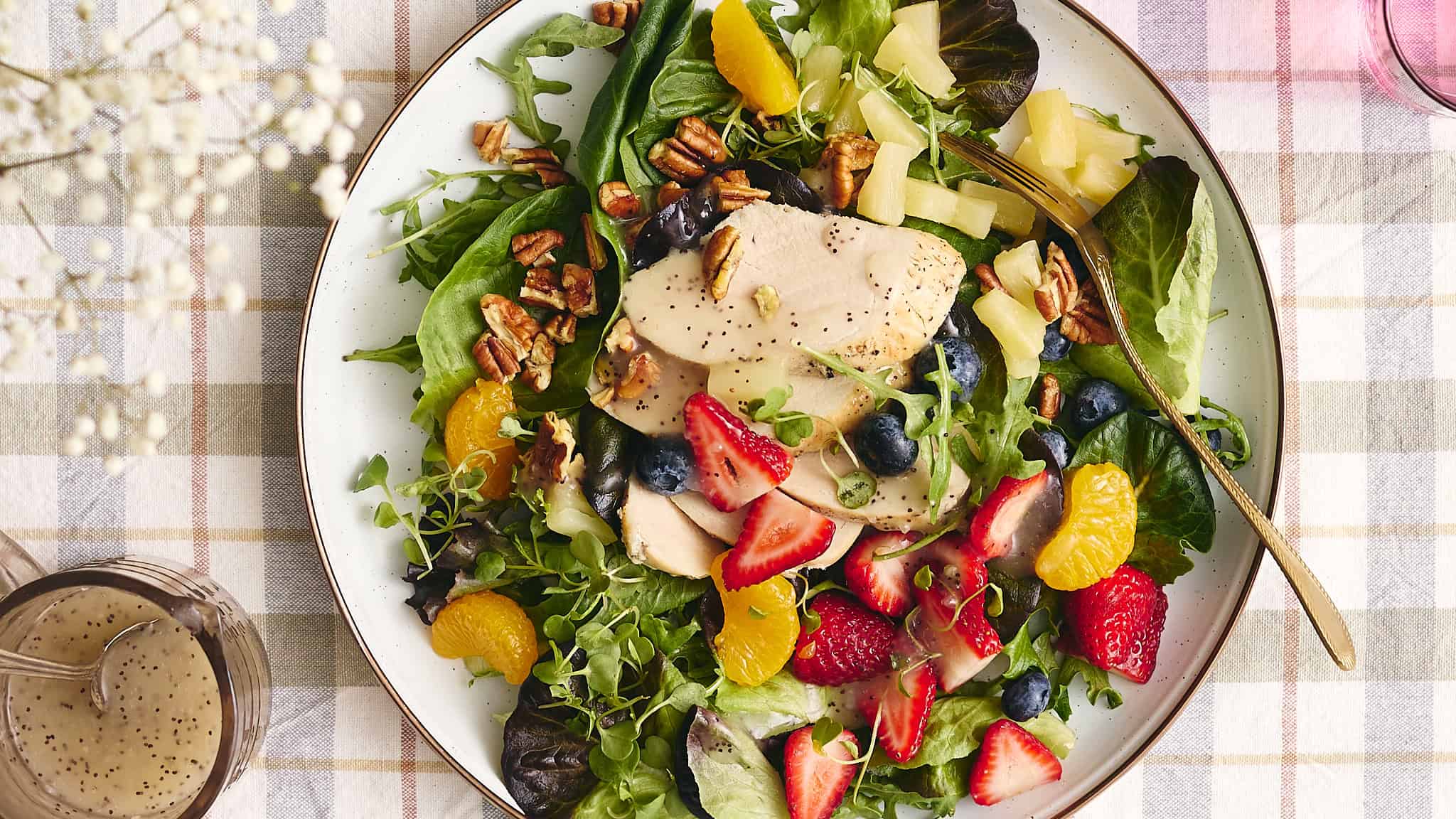 Fresh garden salad with grilled chicken, mixed greens, strawberries, blueberries, mandarin oranges, walnuts, and creamy vinaigrette dressing on a white plate.