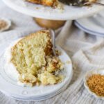 Rich, moist coconut cake with creamy frosting and toasted coconut flakes on top, served on a vintage white plate with a rustic cafe vibe, perfect for dessert or special occasions.