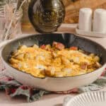 Savory breakfast casserole with eggs, potatoes, sausage, and cheese in a white skillet on a rustic kitchen countertop.