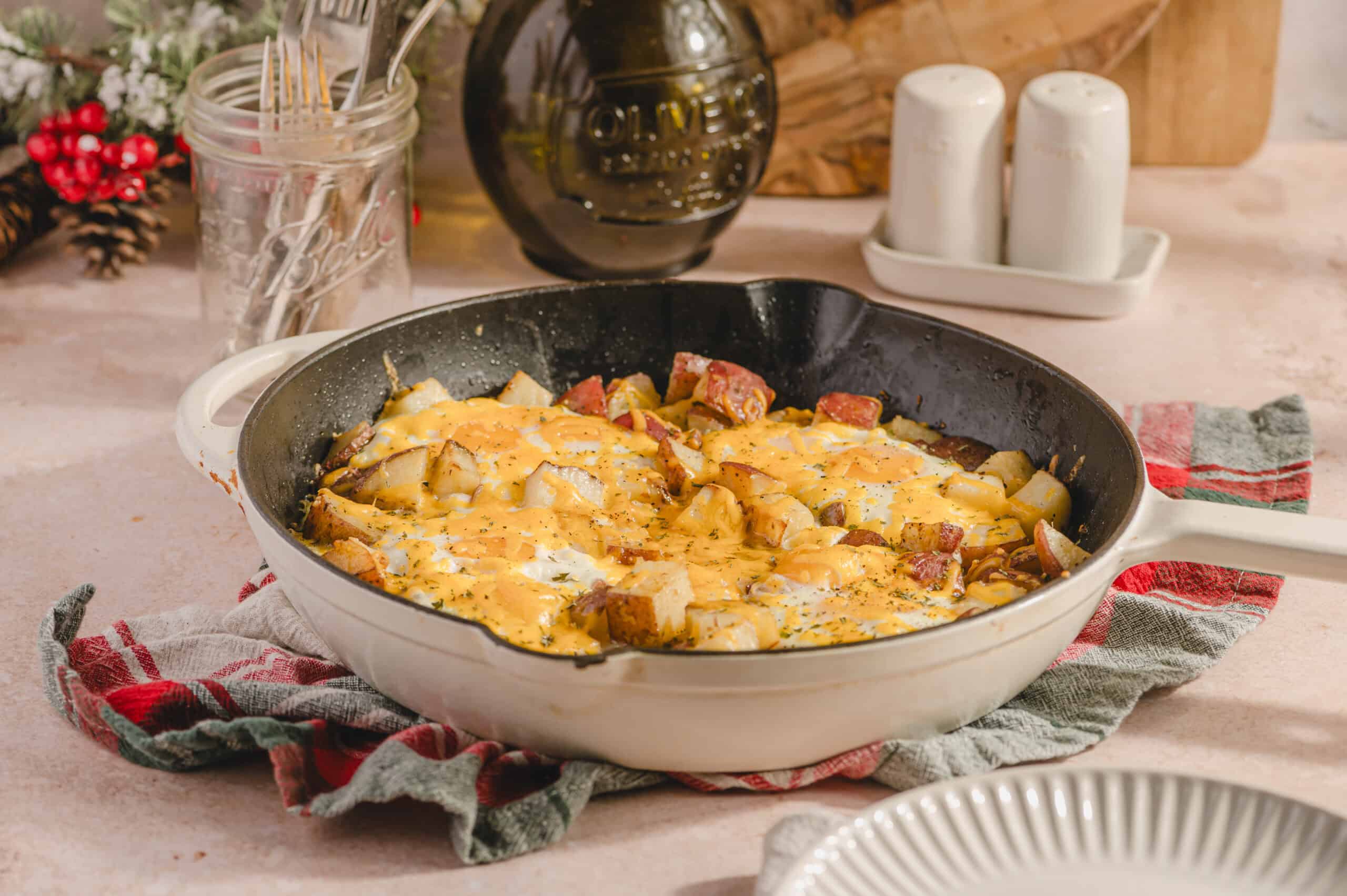 Savory breakfast casserole with eggs, potatoes, sausage, and cheese in a white skillet on a rustic kitchen countertop.
