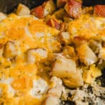 Juicy breakfast skillet with eggs, diced potatoes, ham, and melted cheese close-up. Perfect for breakfast, brunch, or hearty morning meals with savory flavors.
