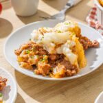 Savory shepherd's pie topped with mashed potatoes and sprinkled with chopped chives, served on a white plate for a hearty comfort food meal.