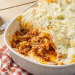Comfort food classic Shepherd's Pie with mashed potato topping and savory ground meat filling, served in a white casserole dish for a hearty family meal.