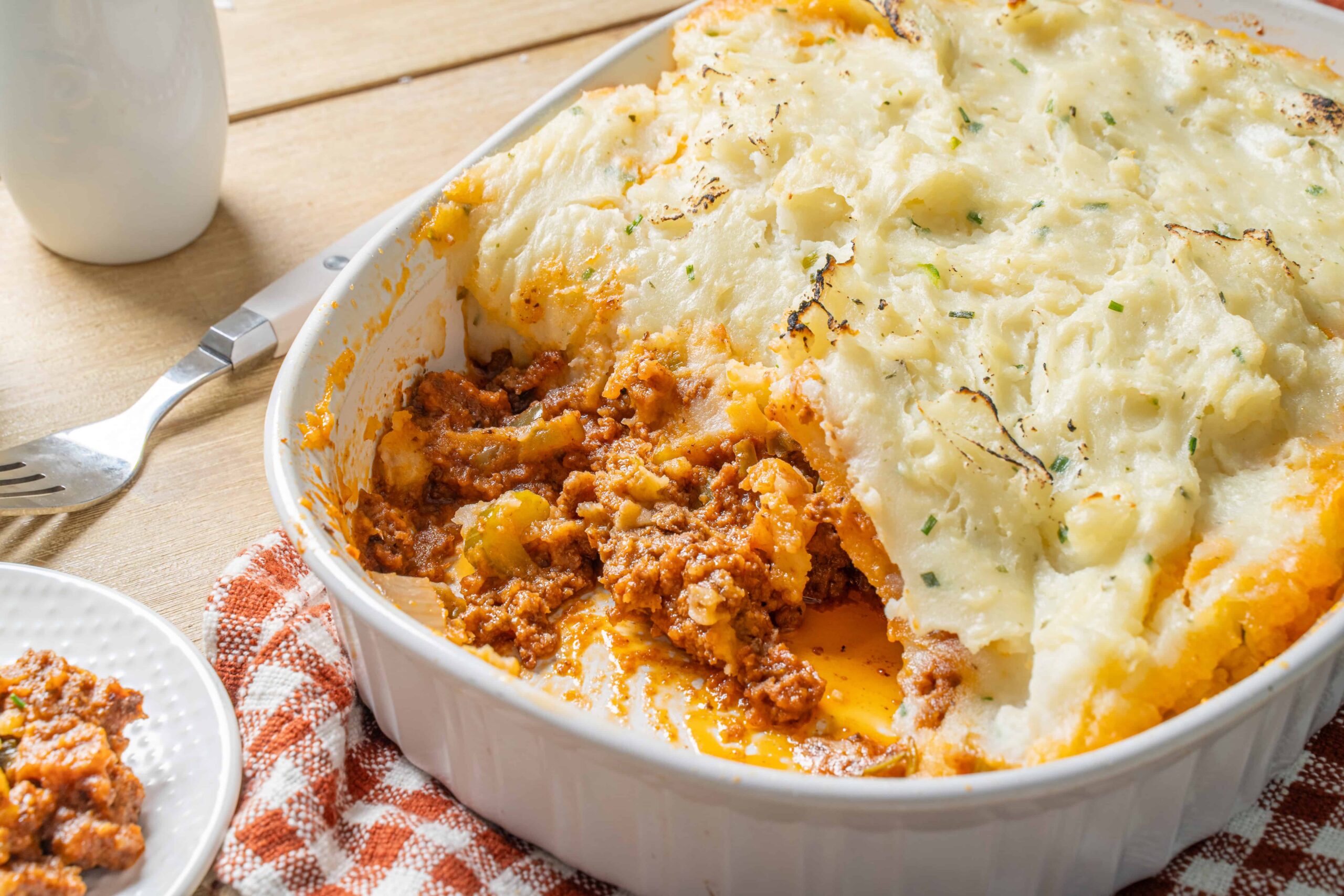 Comfort food classic Shepherd's Pie with mashed potato topping and savory ground meat filling, served in a white casserole dish for a hearty family meal.