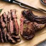 Juicy, perfectly cooked steak sliced and served on a wooden cutting board with fresh herbs and peppercorns, ideal for steak lovers and barbecue enthusiasts.