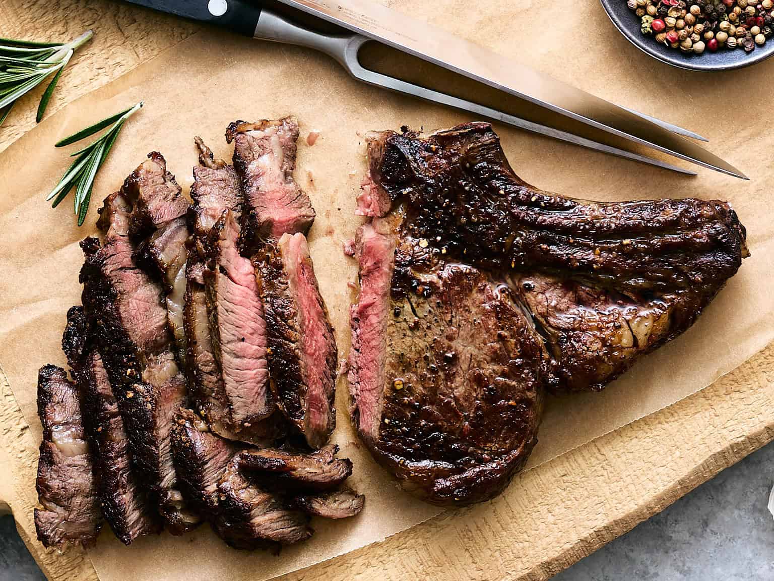 Juicy, perfectly cooked steak sliced and served on a wooden cutting board with fresh herbs and peppercorns, ideal for steak lovers and barbecue enthusiasts.