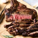 Juicy, perfectly cooked medium-rare steak with a seared crust on a wooden cutting board, sliced to showcase the tender, flavorful interior, ready to serve as a delicious main course.