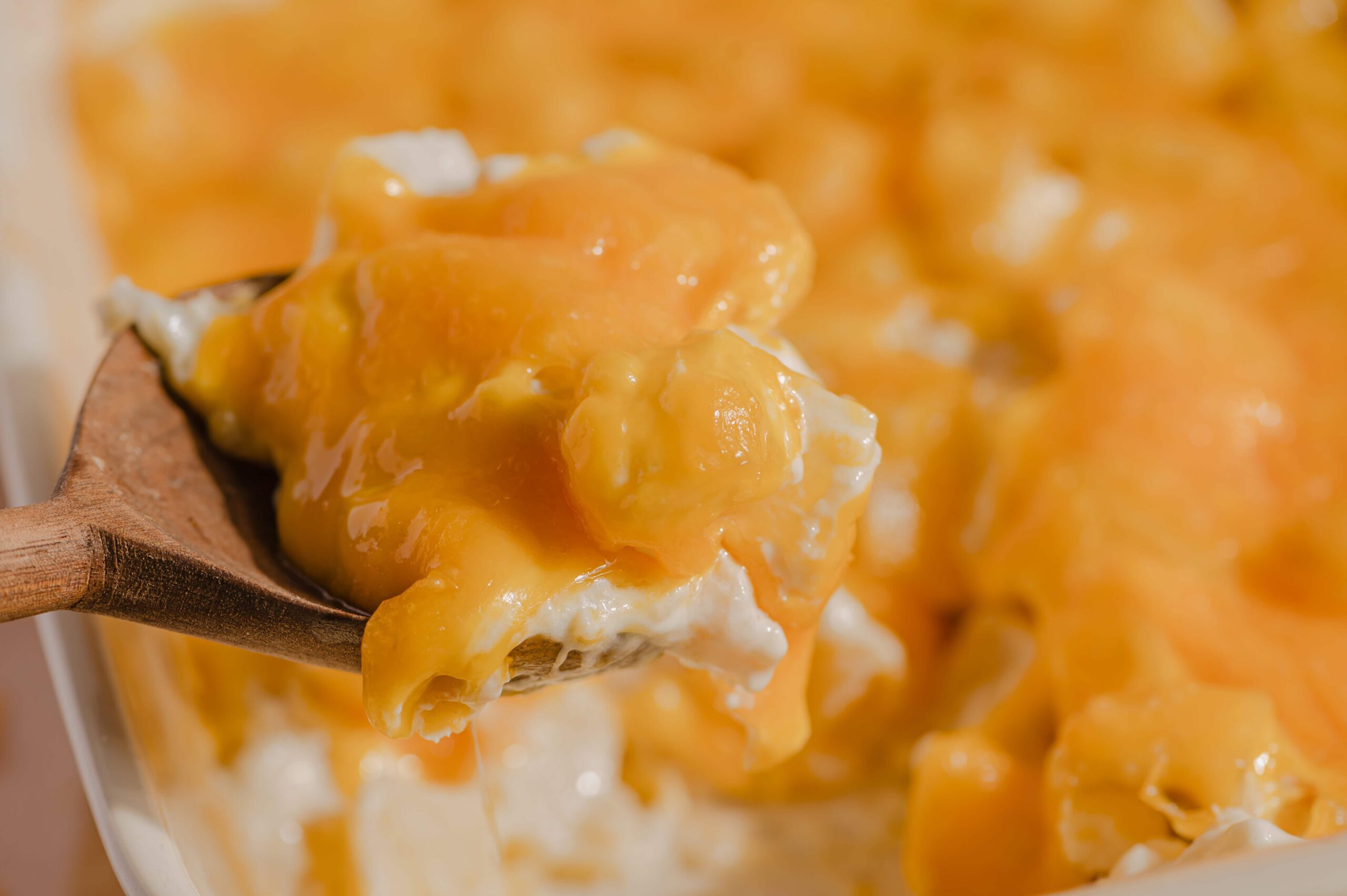 Creamy cheesy macaroni and cheese served in a white bowl with a wooden spoon, showcasing melted cheddar cheese, smooth sauce, and tender pasta, perfect comfort food for all ages.