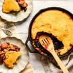 Rich, golden cornbread casserole with bean and sausage filling served in a cast iron skillet, with slices on decorative plates, perfect comfort food for family dinner.