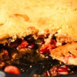 Golden brown fruit pie with a slice removed, showing a rich, fruity filling with cherries and berries inside. Freshly baked pie resting in a baking dish, perfect for dessert or special occasions.