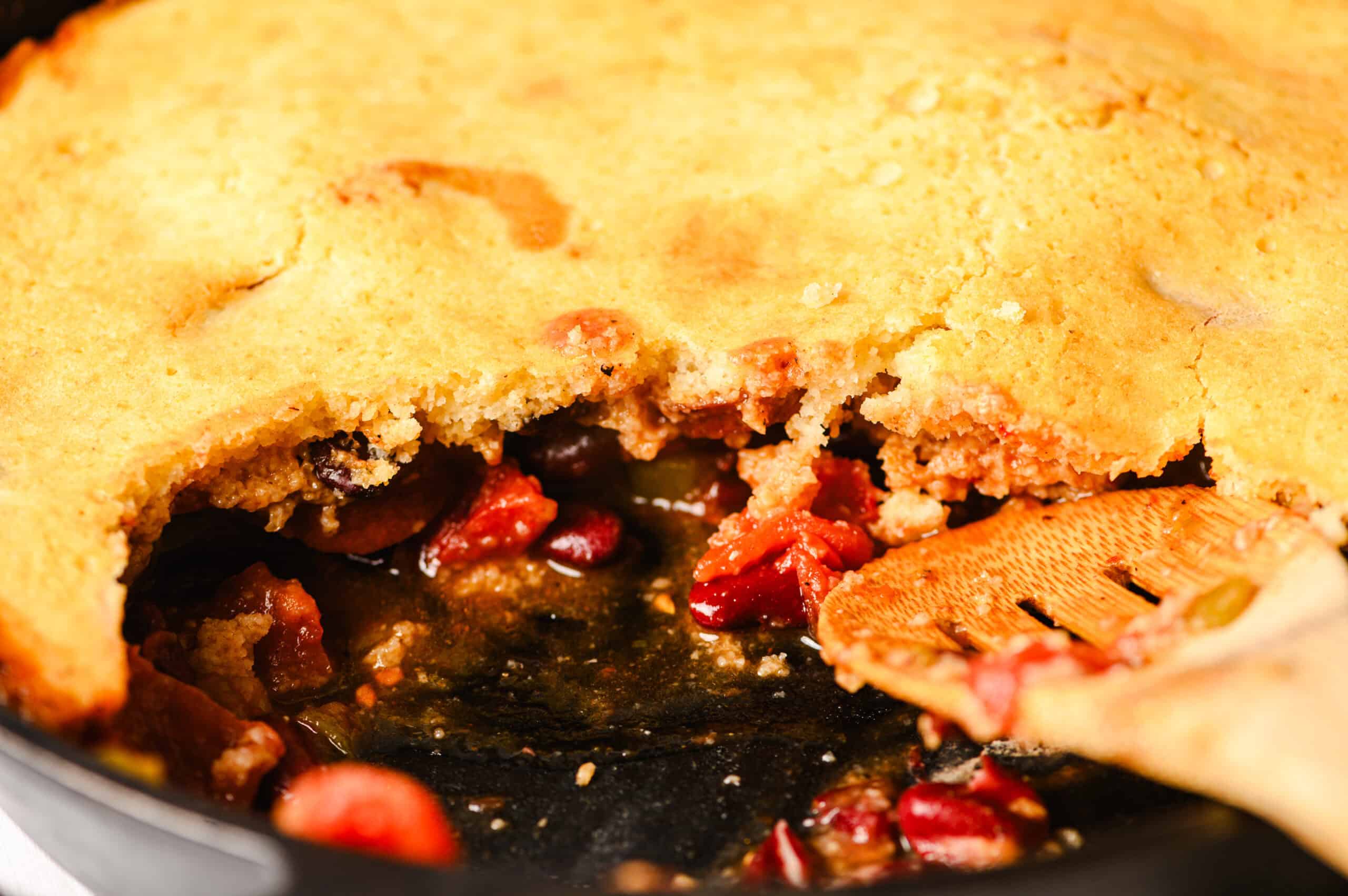 Golden brown fruit pie with a slice removed, showing a rich, fruity filling with cherries and berries inside. Freshly baked pie resting in a baking dish, perfect for dessert or special occasions.