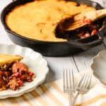Creamy sausage and vegetable casserole served with a slice on decorative plates, fresh out of a cast-iron skillet, garnished with rich tomato sauce and crispy toppings, perfect for comforting meals.
