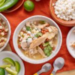 Fresh Mexican pozole with shredded chicken, hominy, and colorful toppings on rustic plates, served with lime wedges and spicy peppers for authentic flavor.