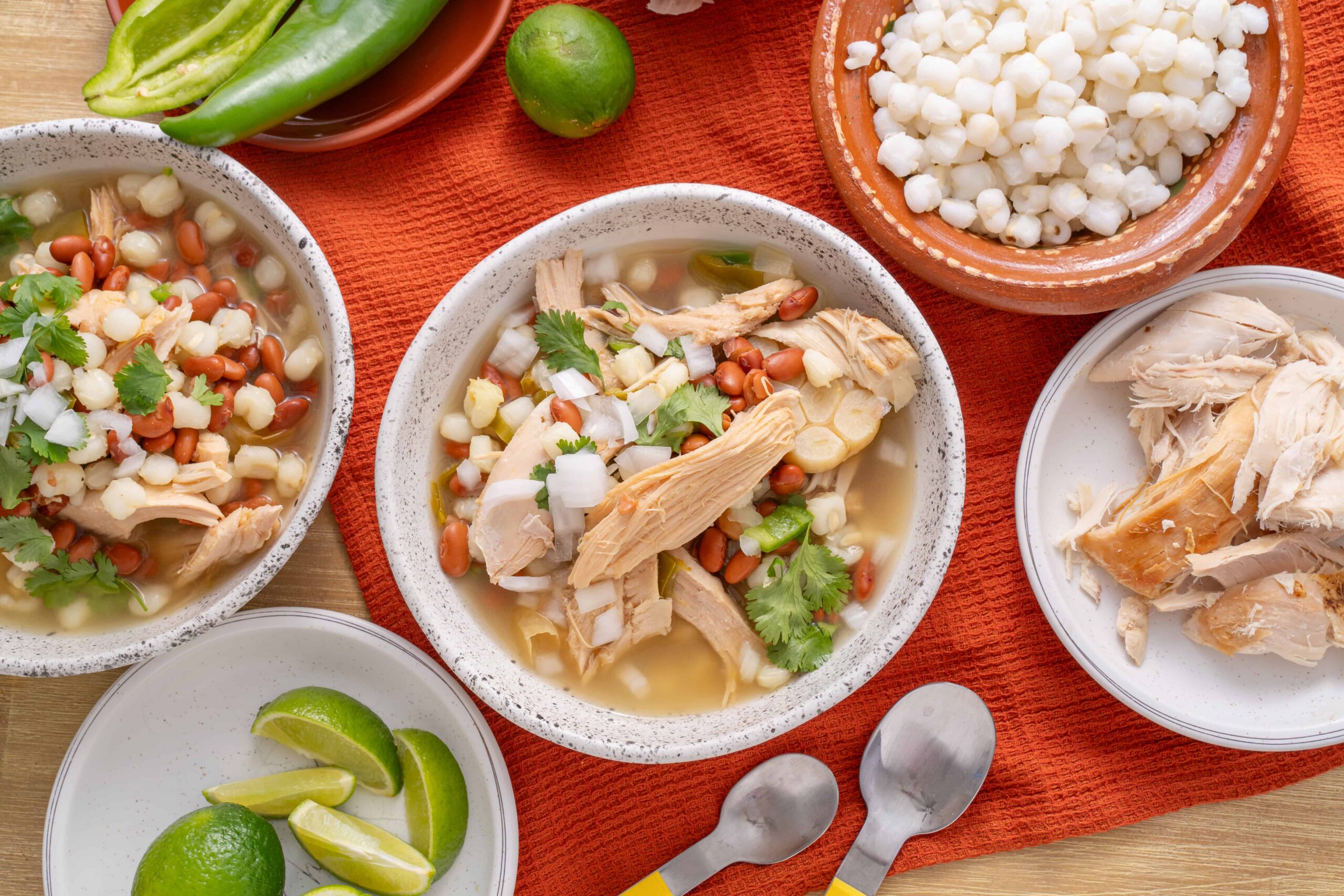 Fresh Mexican pozole with shredded chicken, hominy, and colorful toppings on rustic plates, served with lime wedges and spicy peppers for authentic flavor.
