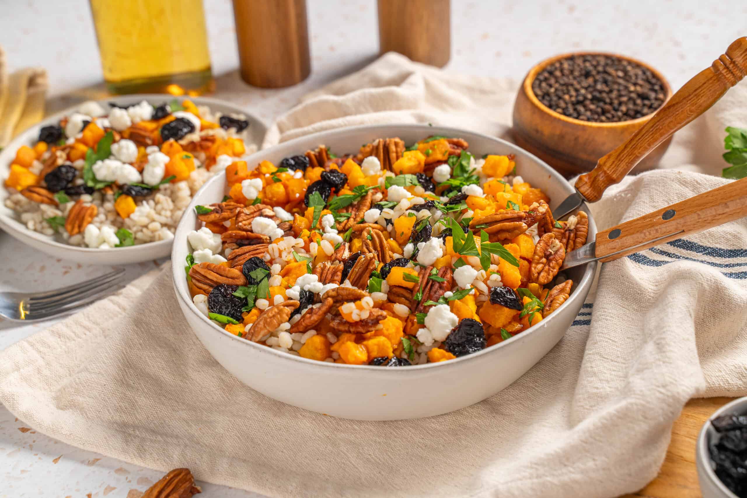 Savory holiday farro salad with roasted sweet potatoes, pecans, dried cranberries, feta cheese, and fresh herbs in a white serving bowl, styled for a cozy, rustic kitchen setting.