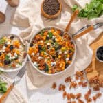 Savory vegan salad with roasted sweet potatoes, pecans, blackberries, crumbled feta, and fresh herbs in a white bowl, served with herbs and bowls of berries on a rustic wooden table.