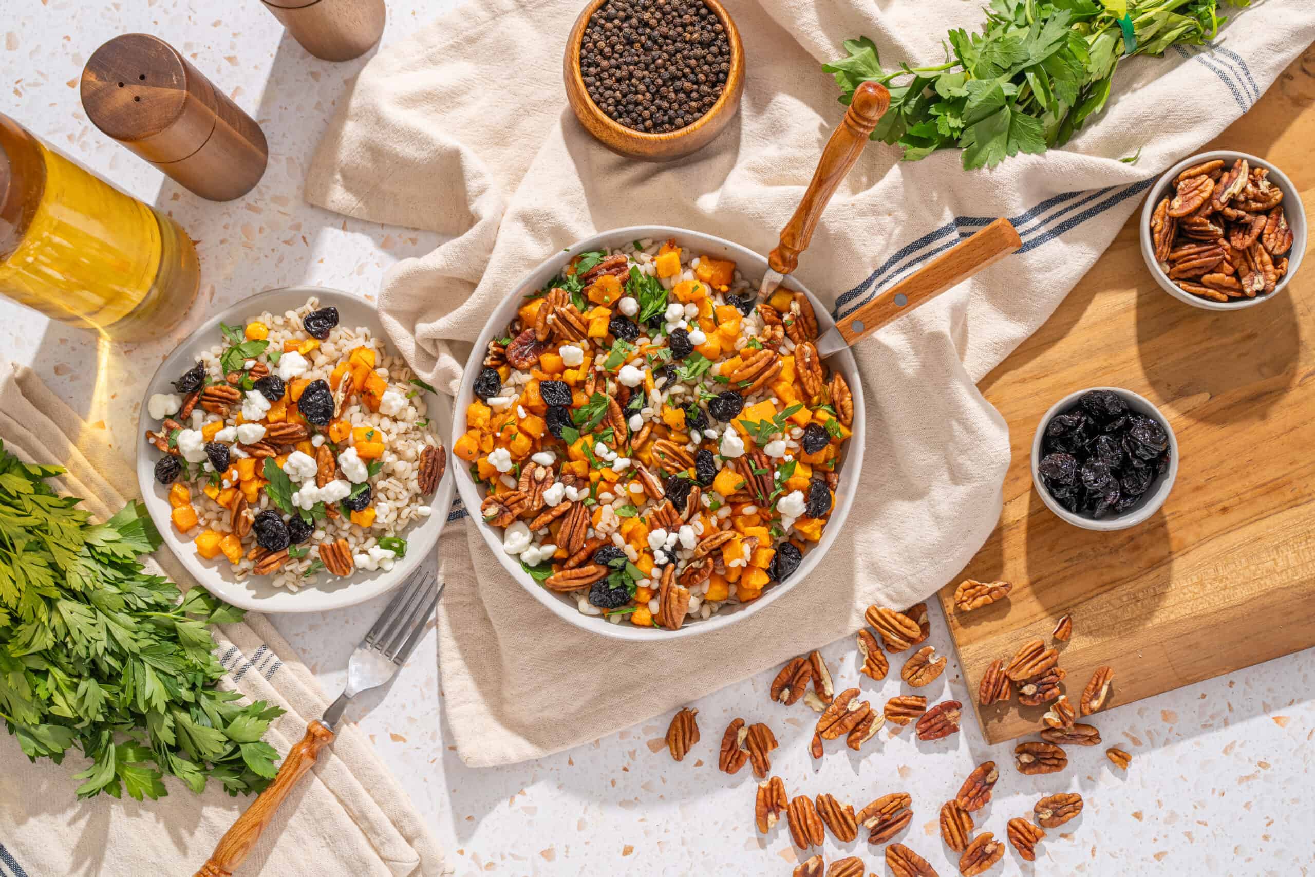 Savory vegan salad with roasted sweet potatoes, pecans, blackberries, crumbled feta, and fresh herbs in a white bowl, served with herbs and bowls of berries on a rustic wooden table.