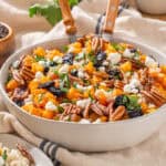 Roasted butternut squash, pecans, cranberries, goat cheese, and fresh herbs salad in a white serving bowl.