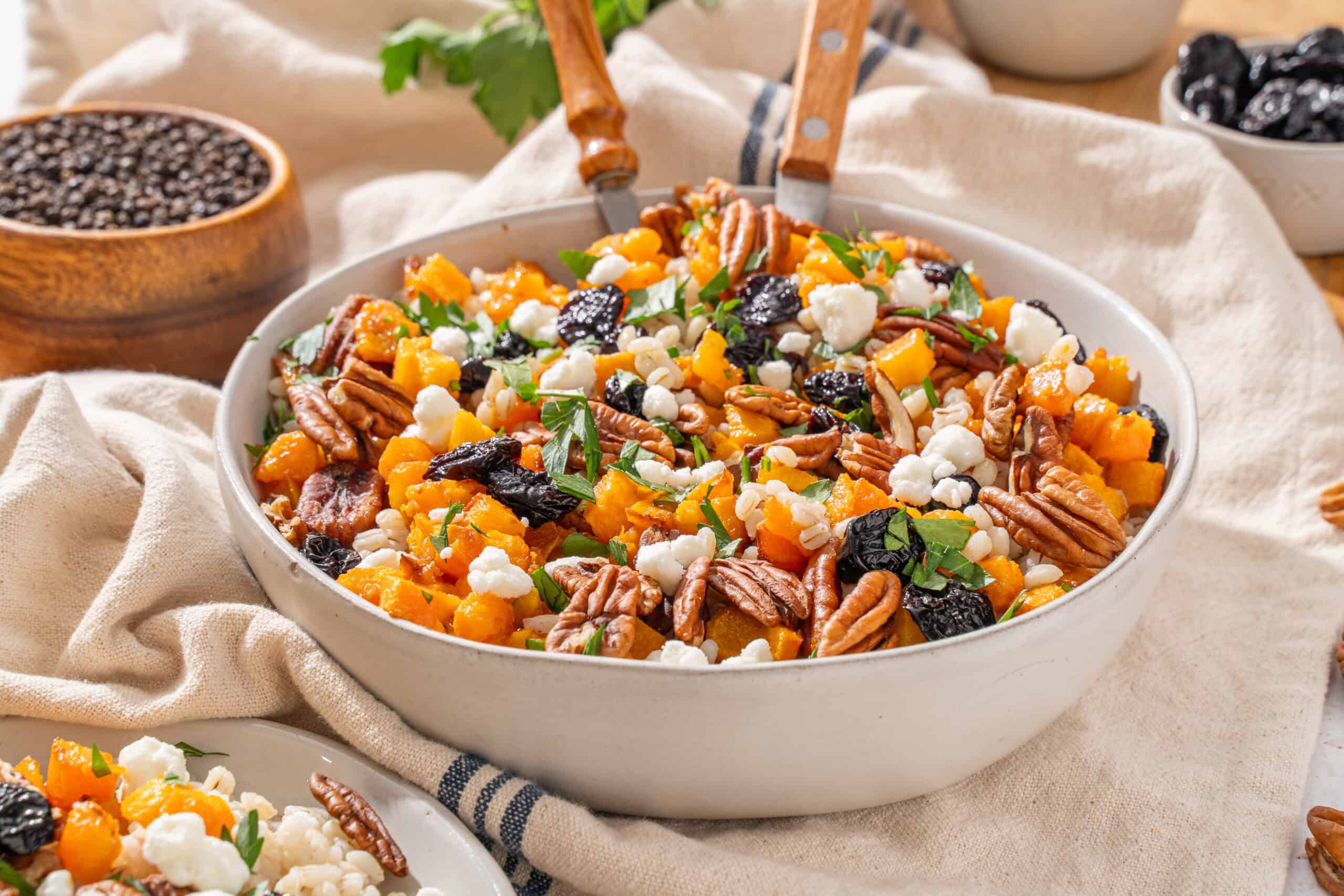 Roasted butternut squash, pecans, cranberries, goat cheese, and fresh herbs salad in a white serving bowl.