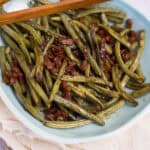 Sautéed green beans with crispy bacon served in a teal ceramic dish, garnished with chopsticks for a flavorful and easy-to-make healthy recipe perfect for dinner or lunch.