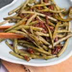 Green beans with bacon, garlic, and herbs in a white dish.