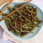 Green beans with bacon, cooked to perfection, on a light blue plate, garnished with crispy bacon pieces. A delicious and savory vegetable dish perfect for side meals or family dinners.
